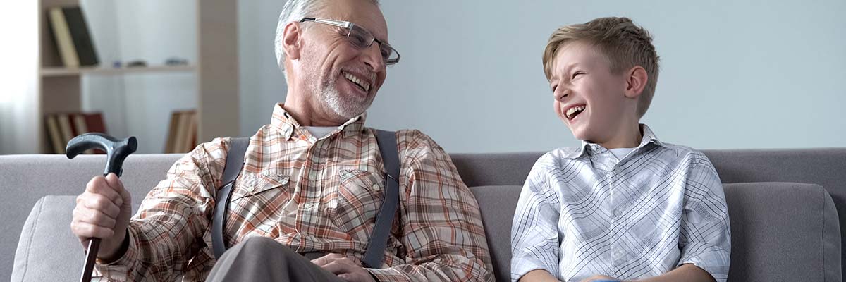 Großvater u. Enkel sitzen auf der Couch und lachen.